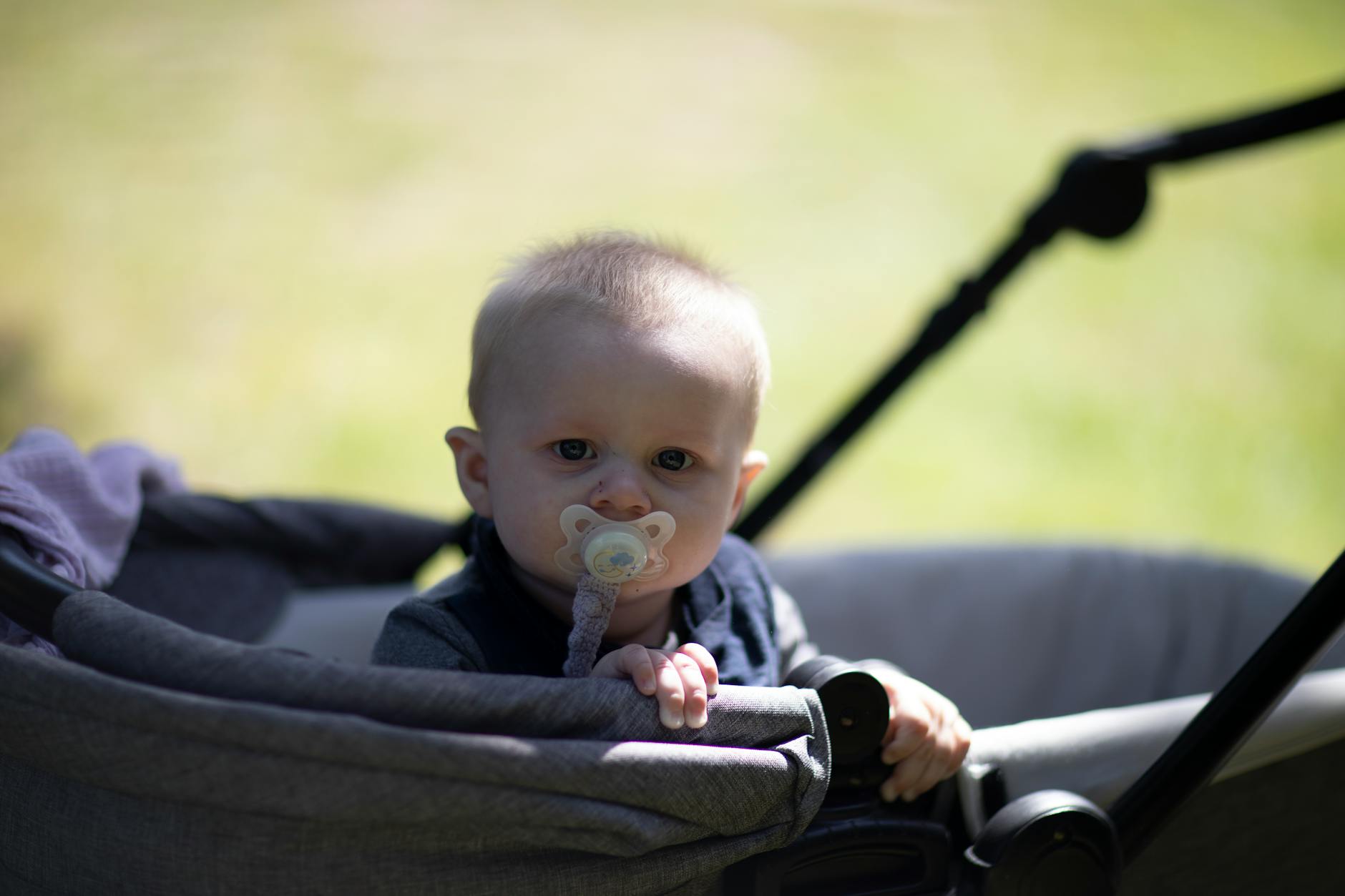 Niemowlę siedzące w spacerówce z smoczkiem podczas spaceru w parku