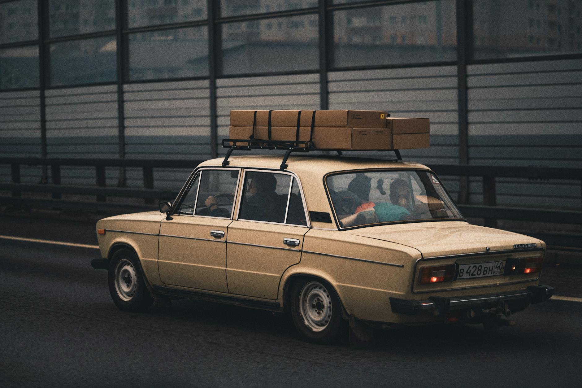 Beżowy sedan z boxem dachowym jedzie autostradą obok miasta