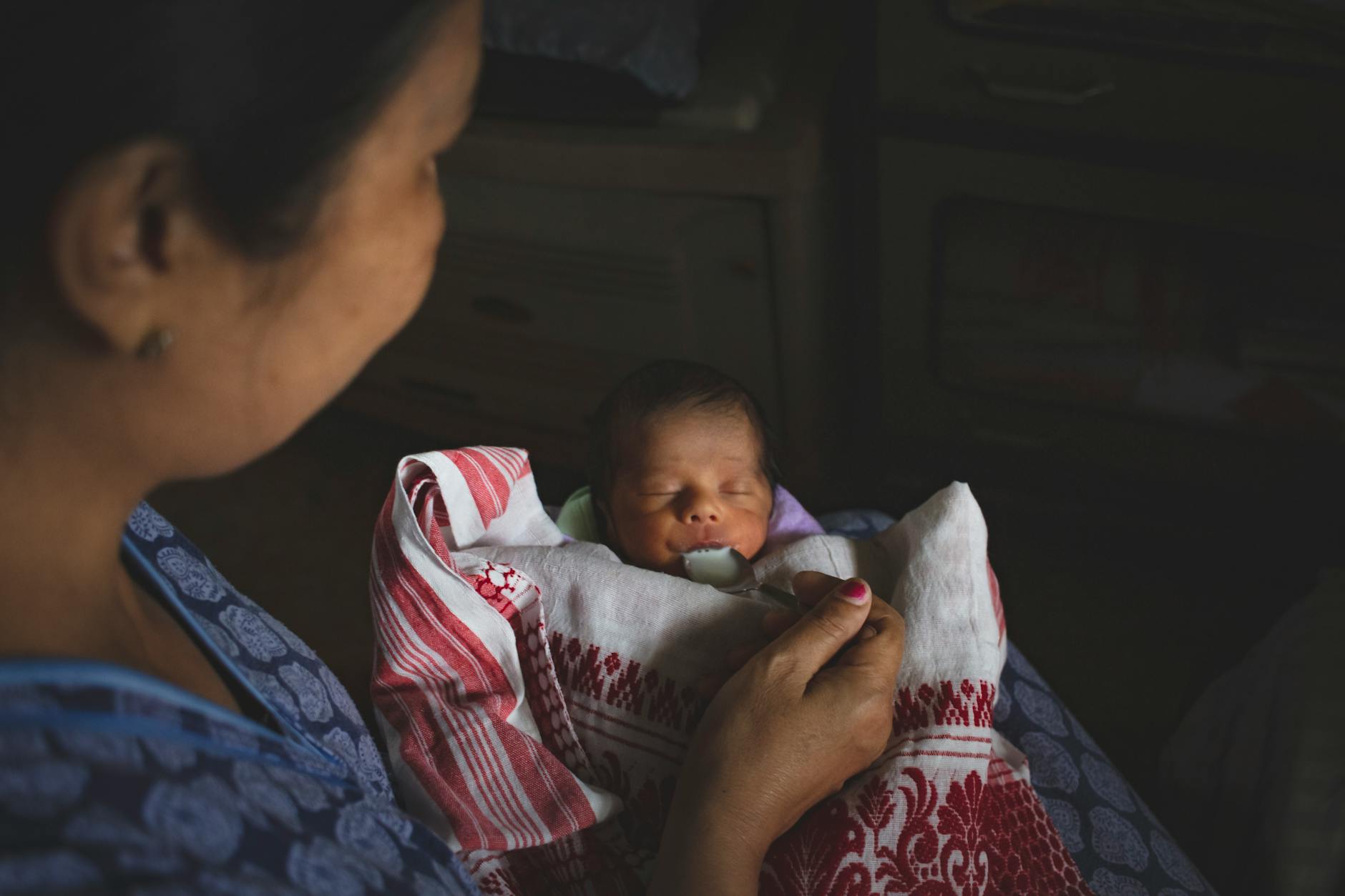 Mama karmi noworodka łyżeczką, otulonego ciepłym kocykiem