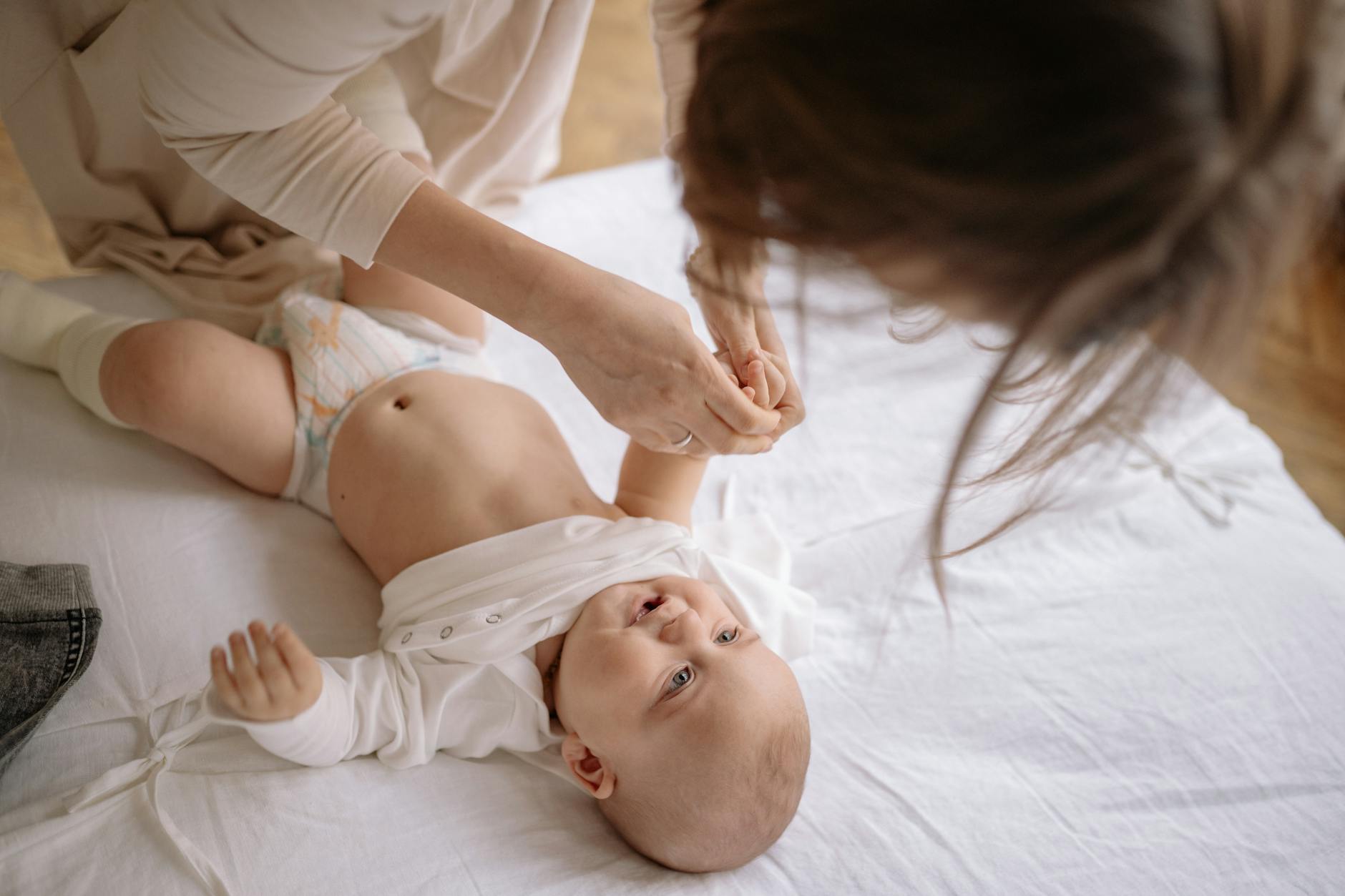 Mama przebiera niemowlę w body w przytulnym domowym wnętrzu