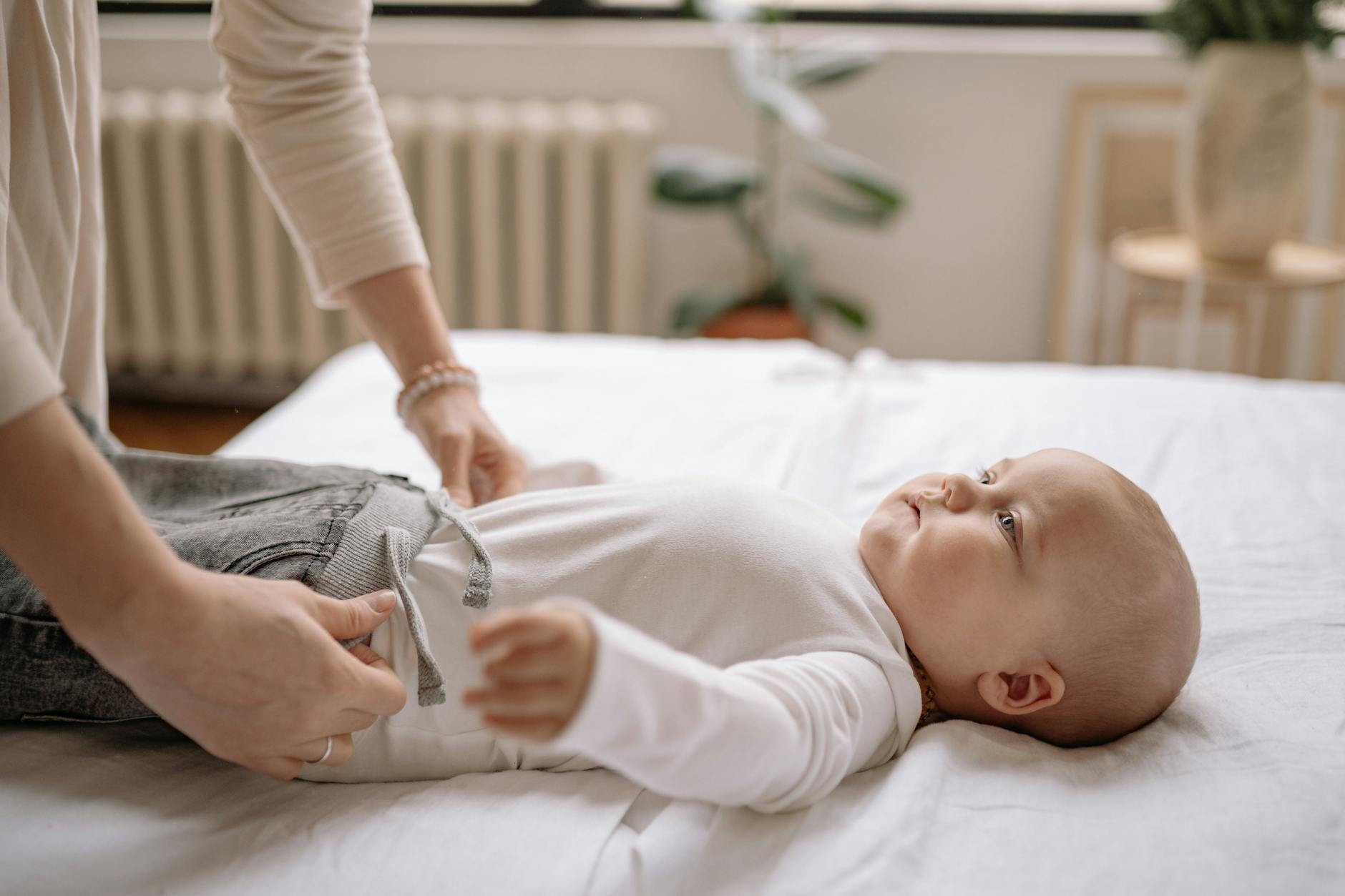 10 sprytnych trików, które sprawią, że codzienne przebieranie malucha będzie prostsze Mama ubiera niemowlę na łóżku, delikatna chwila codziennej pielęgnacji