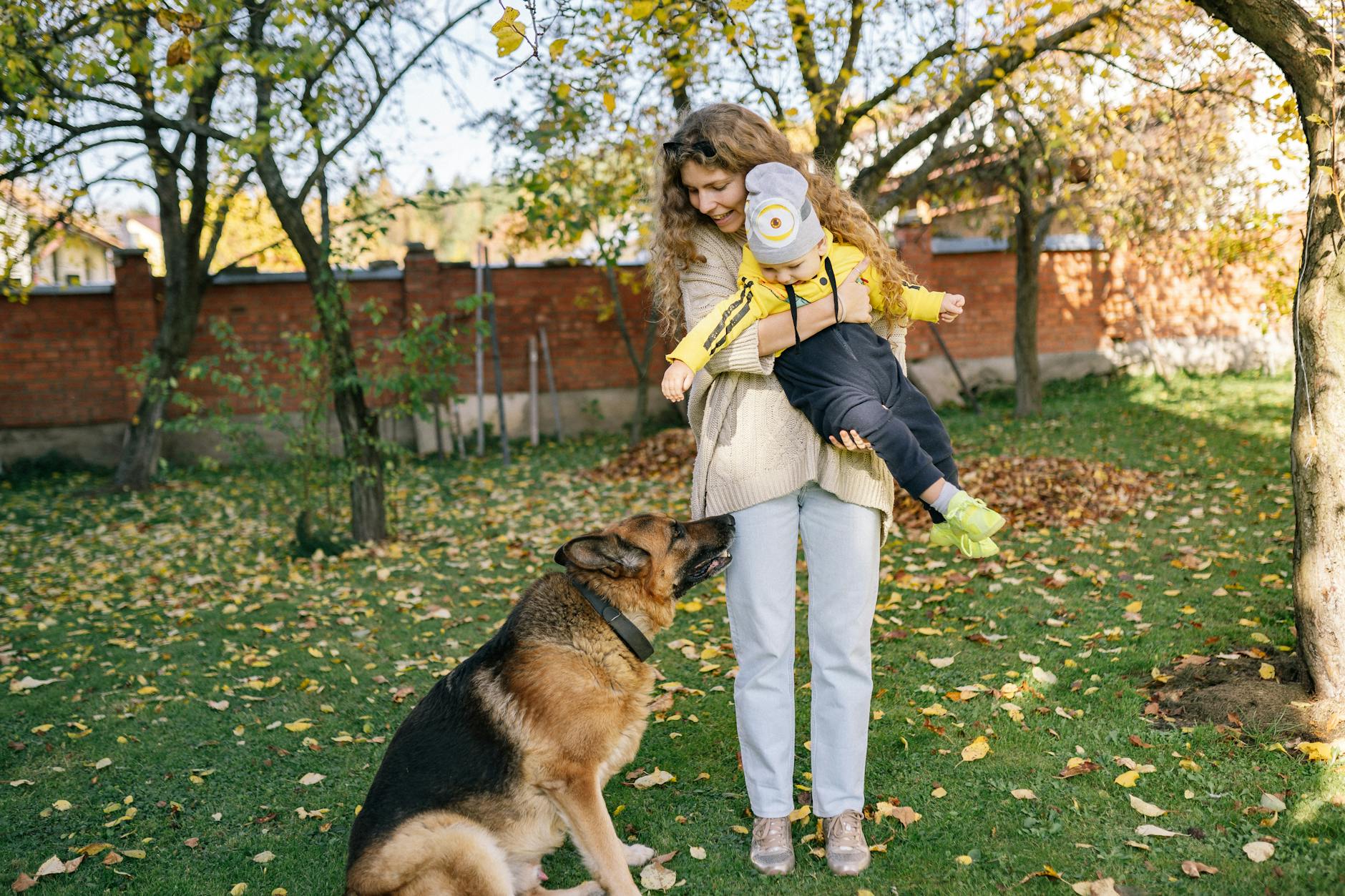 Mama z dzieckiem na jesiennym podwórku obok spokojnie siedzącego psa