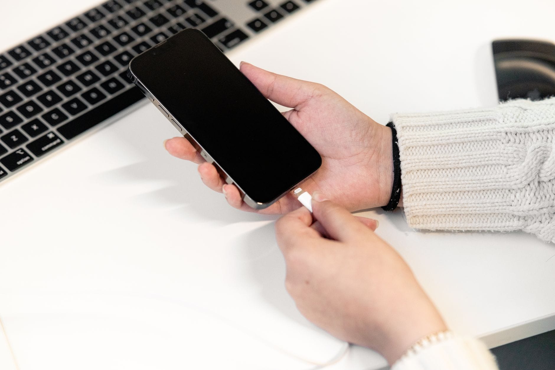 Kobieta podłącza smartfon do ładowarki przy biurku obok laptopa