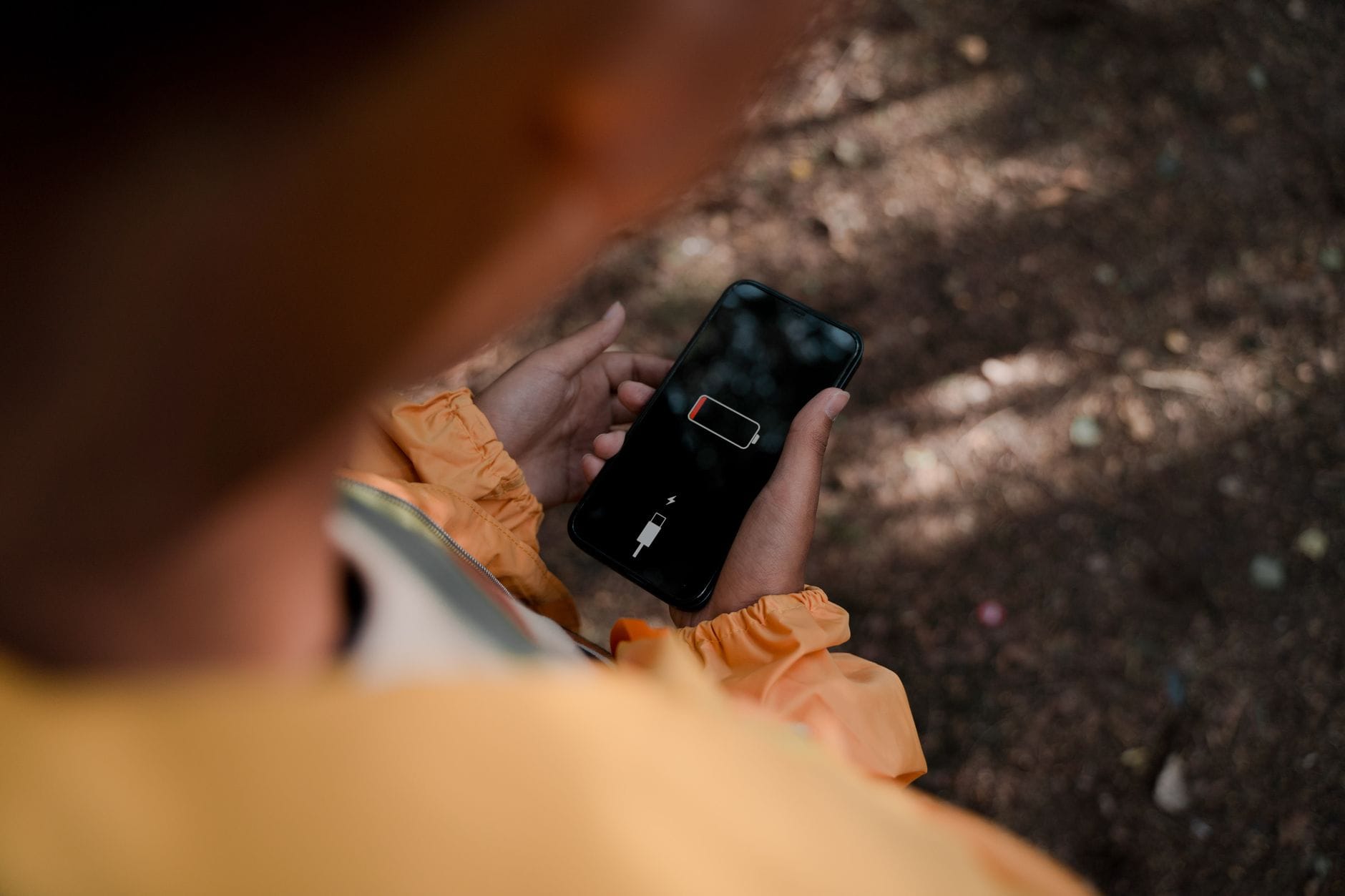 Jak dbać o baterię w smartfonie, aby dłużej działała i nie wymagała szybkiej wymiany Nastolatek w lesie trzyma smartfon z ikoną niskiego poziomu baterii