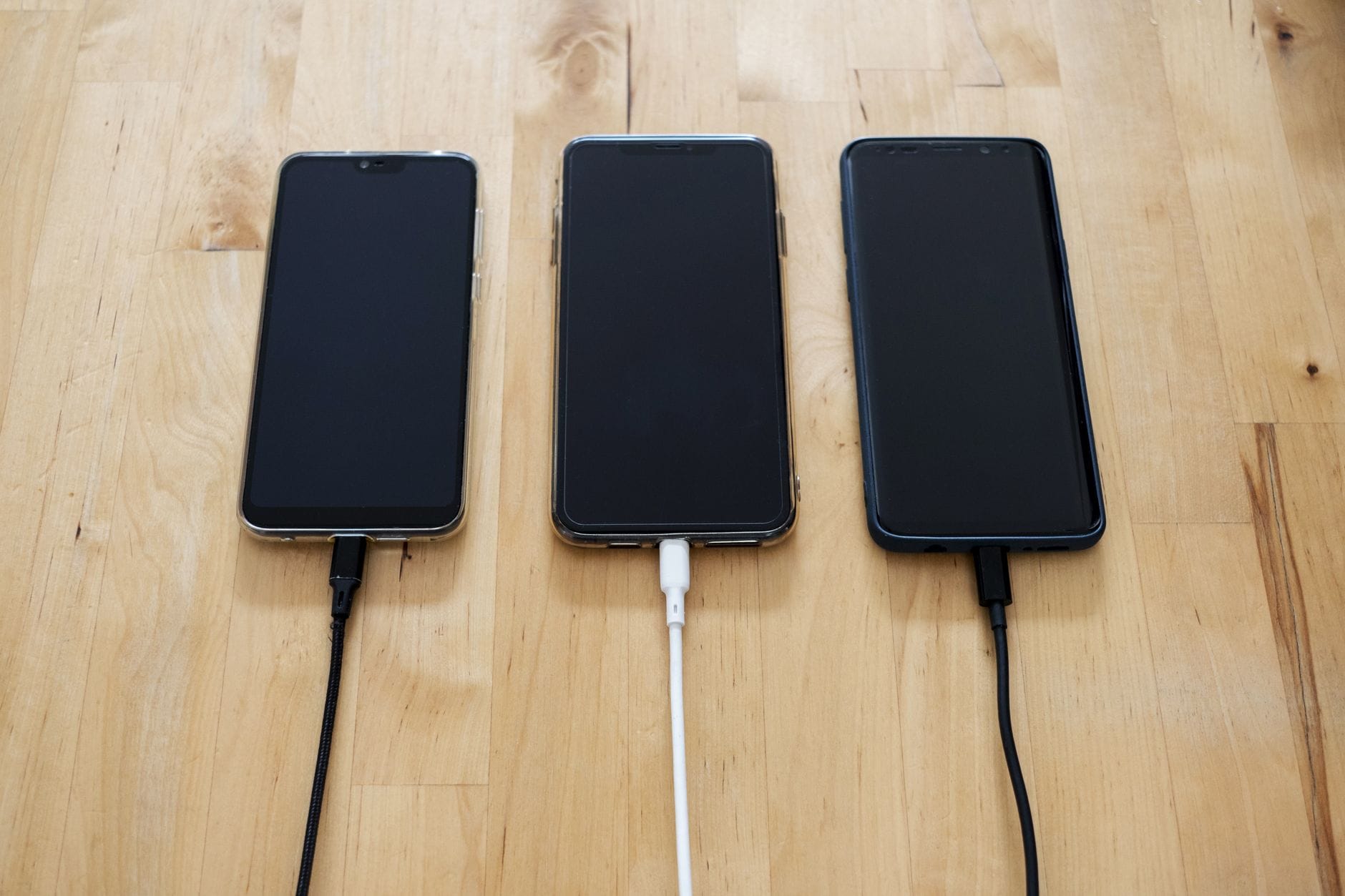 Trzy smartfony podłączone do ładowarek na drewnianym blacie
