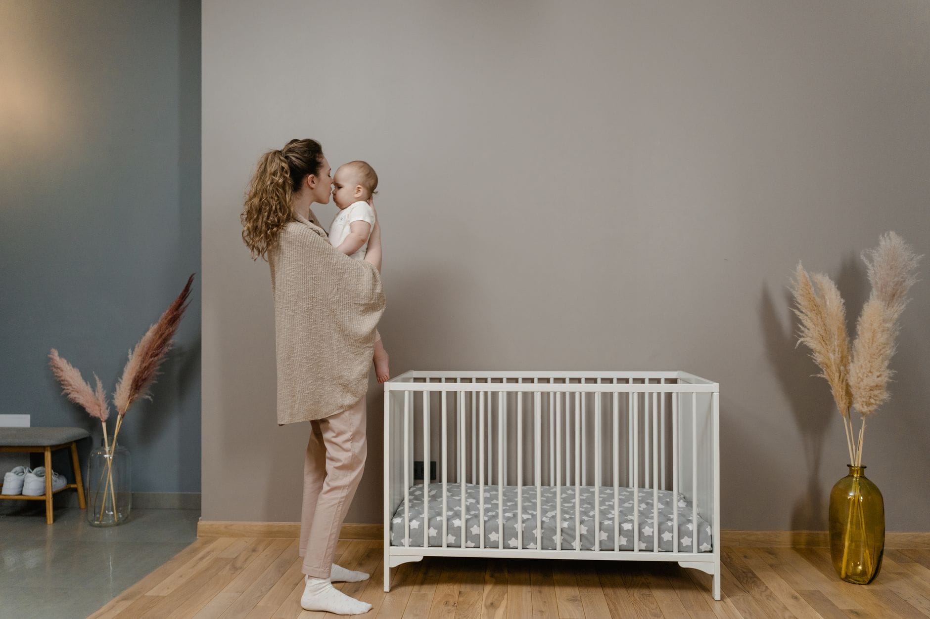 Mama trzyma niemowlę obok łóżeczka w przytulnym pokoju dziecięcym